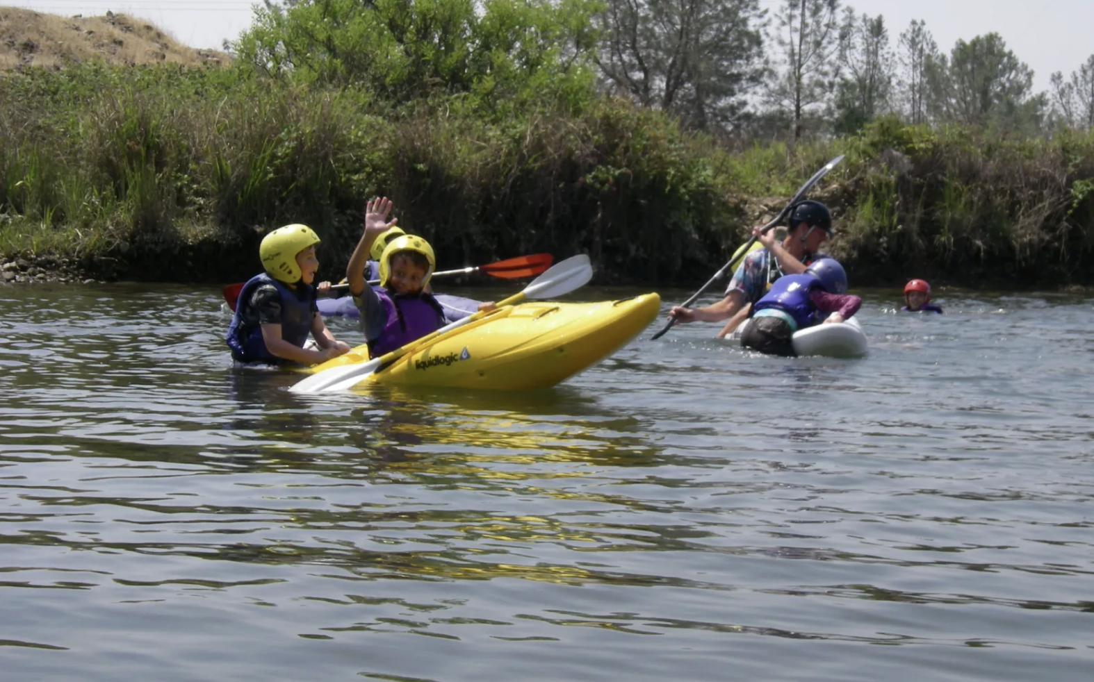 Kids learning to kayak in helmets and life vests on the river